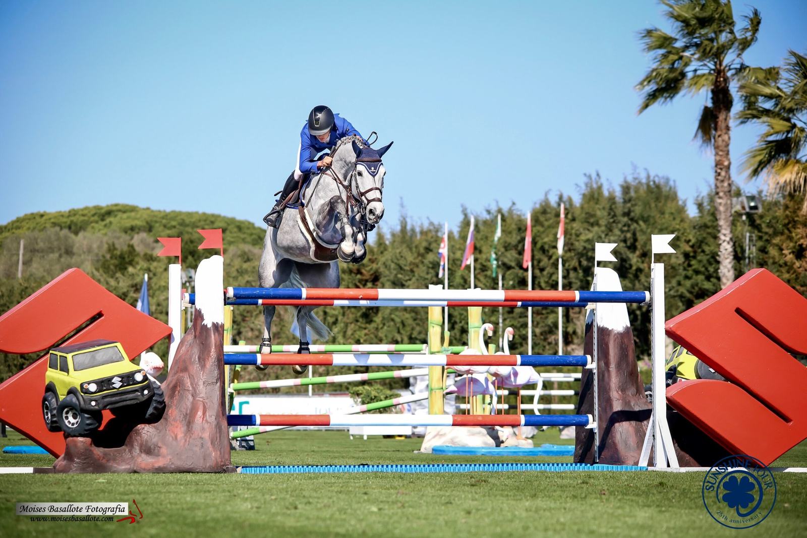 Diana saltando con un caballo tordo en el Sunshine Tour, bajo un cielo azul con palmeras