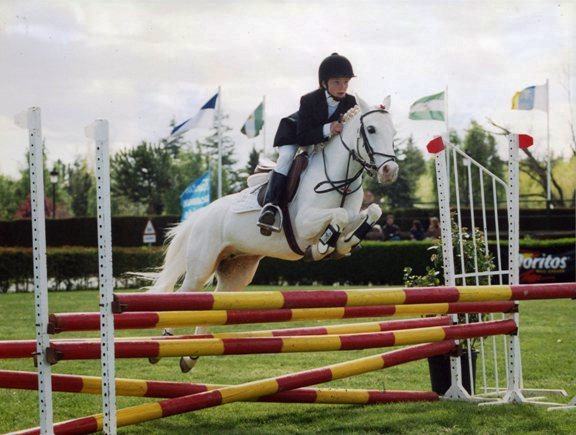 Diana de niña saltando con un poni blanco