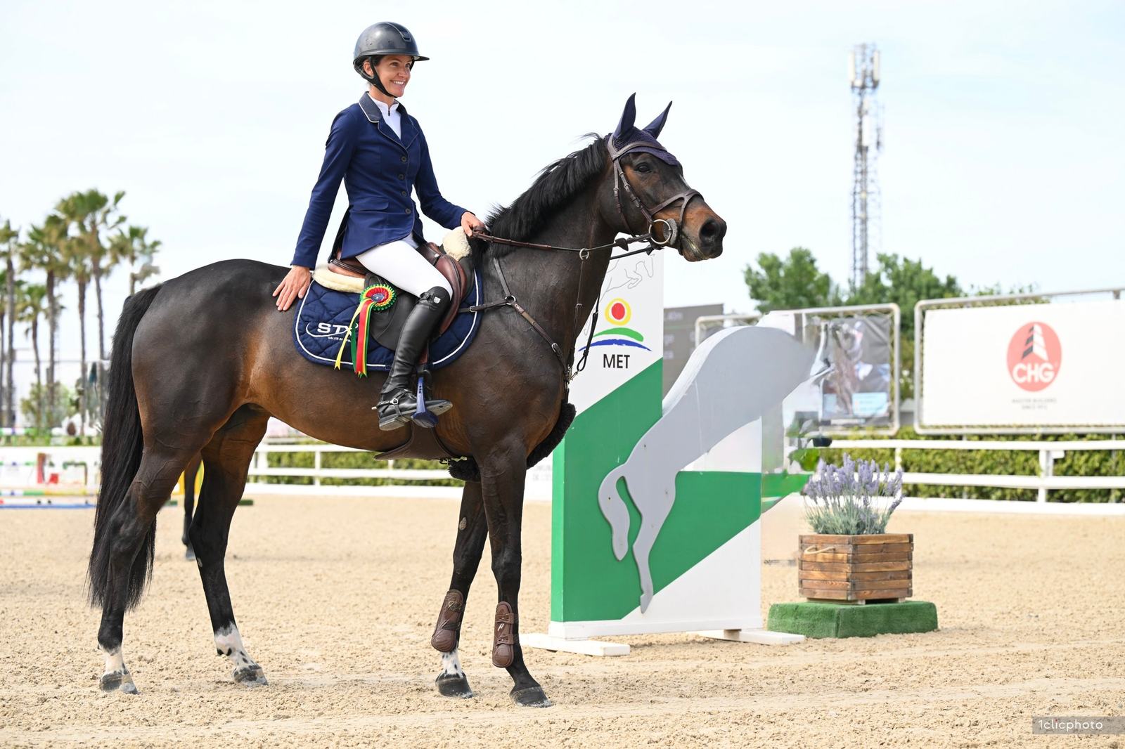 Diana sonriendo a lomos de un caballo castaño oscuro, con una escarapela